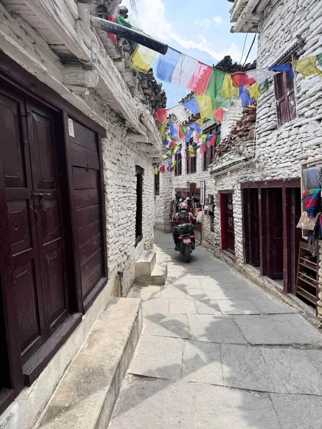Moto traversant un village de pierre décoré de drapeaux de prières