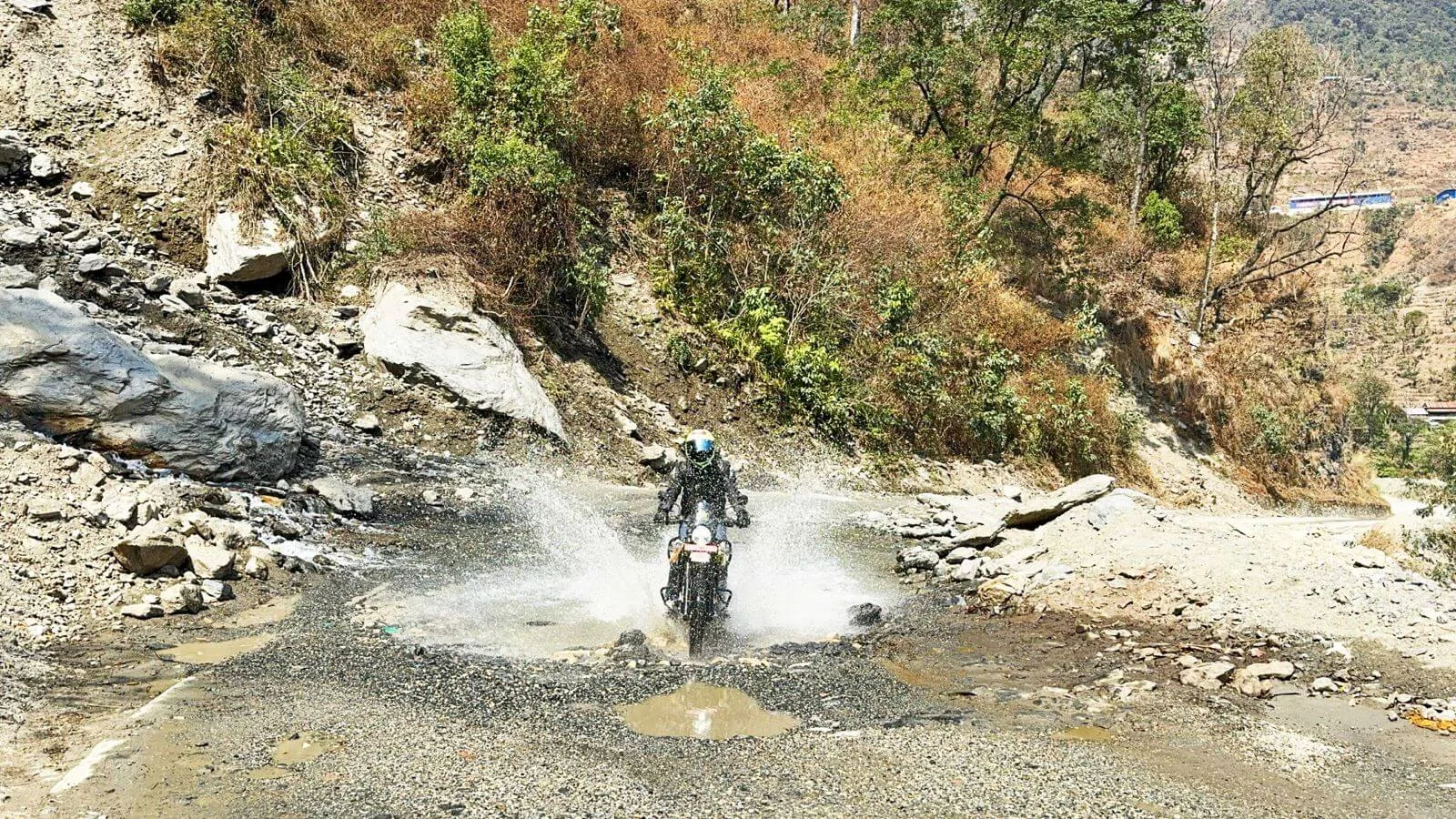 Motard franchissant un passage d’eau sur une piste népalaise